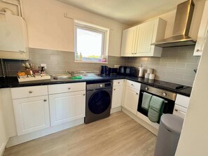 A compact kitchen with white cabinets, a built-in washing machine, a microwave, and a stove. - 2-Bed Milton Keynes Maisonette Parking (Milton Keynes)