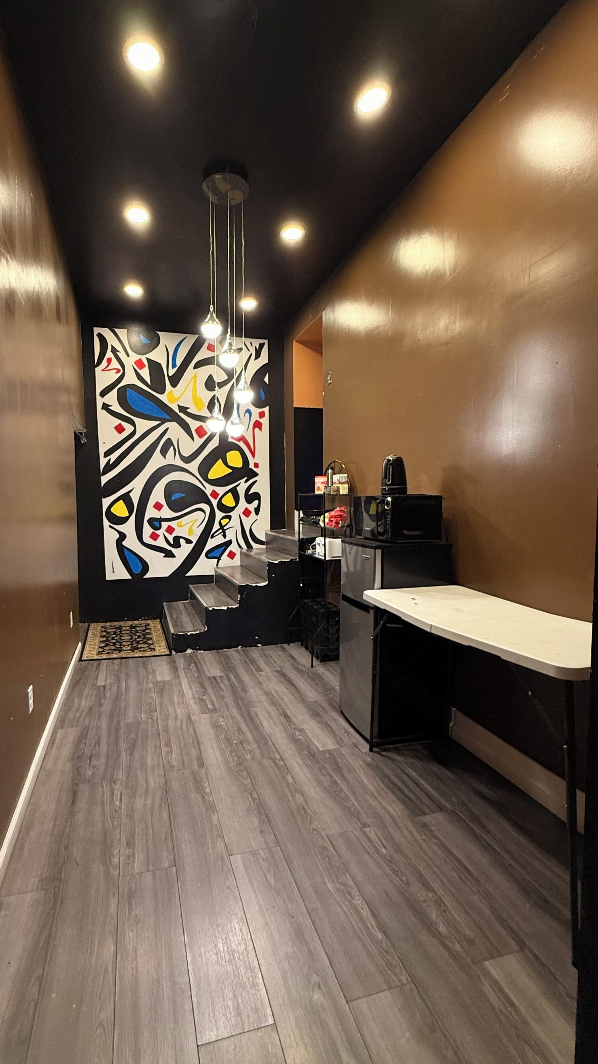 A modern kitchen with a wooden floor, a black countertop, and a colorful abstract wall art.
