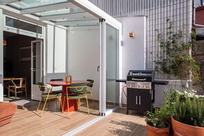 An outdoor patio with a glass door leading to a room, a barbecue grill, and potted plants. - Golden Hour | Luxury 4-Bedroom Home for Families & Groups (Porto)