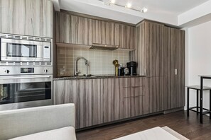 A modern kitchen with wooden cabinetry, a built-in microwave, and a coffee maker. - Stylish 1bed 1 bath Central | Pool | Gym (Toronto)