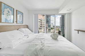 A bedroom with a large bed, a view of buildings through a sliding door, and two framed artworks on the wall. - Stylish 1bed 1 bath Central | Pool | Gym (Toronto)