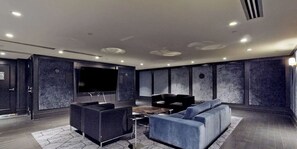 Een modern interieur met een grote flatscreen televisie, donkere banken en een kamerbreed tapijt met een patroon.