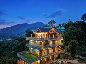 A multi-story building with balconies, a stone facade, and a view of the surrounding landscape. - ELIVAAS Secret Escape Aashiyana 2BHK (Solan)