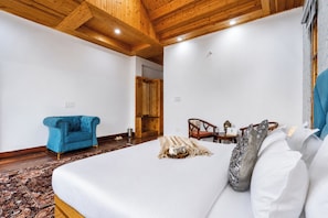Una habitación de hotel con una cama grande, un sillón azul, un armario de madera y una mesita con una silla.
