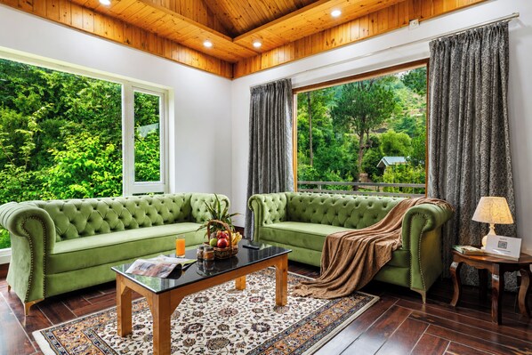 Un sofá verde, una mesa de centro, una alfombra estampada y una ventana con cortinas.