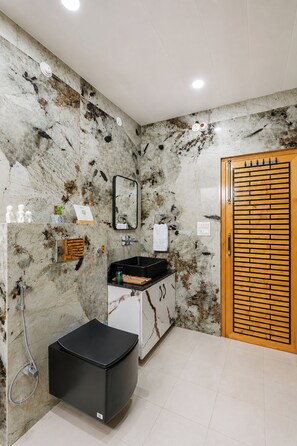 A bathroom with a marble wall, a black sink, a mirror, a wooden door, and a shower area. - ELIVAAS Secret Escape Aashiyana 2BHK (Solan)