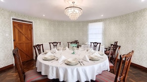 Un comedor con una mesa redonda dispuesta para seis personas, rodeada de sillas de madera, una araña y papel tapiz estampado.