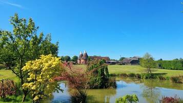 A rural landscape with a pond, trees, and a building with a conical roof.