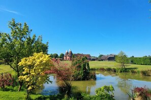 A rural landscape with a pond, trees, and a building with a conical roof. - Sharvels Oast House - Pool, Tennis, Luxury Home (Rye)