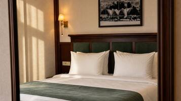 A neatly made bed with a green throw, a wall-mounted lamp, and a framed cityscape picture above it.