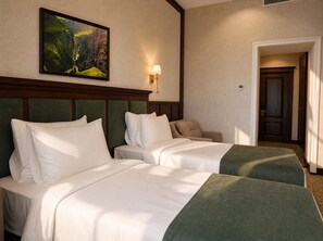 Habitación de hotel con dos camas, un cuadro en la pared, una lámpara y una puerta que da a otra habitación.