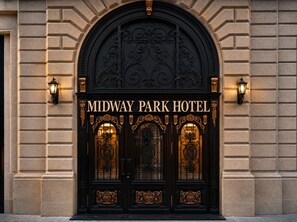 La entrada del Hotel Midway Park, con puertas negras ornamentadas y detalles dorados.