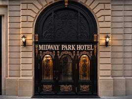 De ingang van het Midway Park Hotel met decoratieve zwarte deuren en gouden accenten.