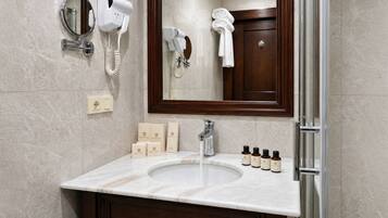 A bathroom with a marble sink, a mirror, a hairdryer, and toiletries.
