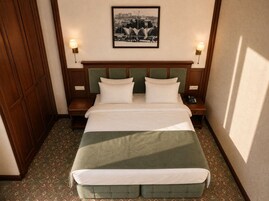 Een hotelkamer met een groot bed, twee nachtkastjes, een lampje en een tapijt met dessin.