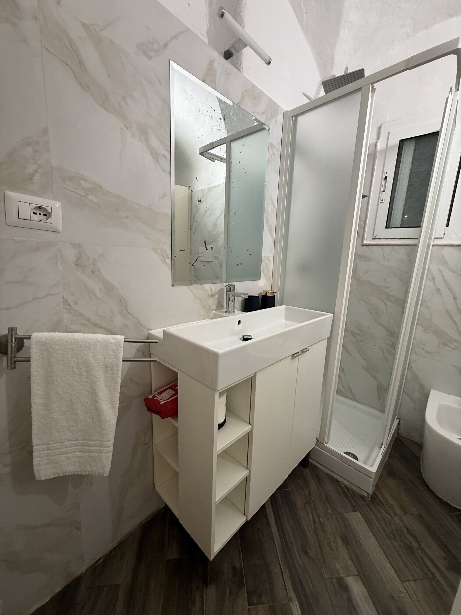 Ein modernes Badezimmer mit weißem Waschtisch, einem Spiegel, einer Duschkabine und einem WC.