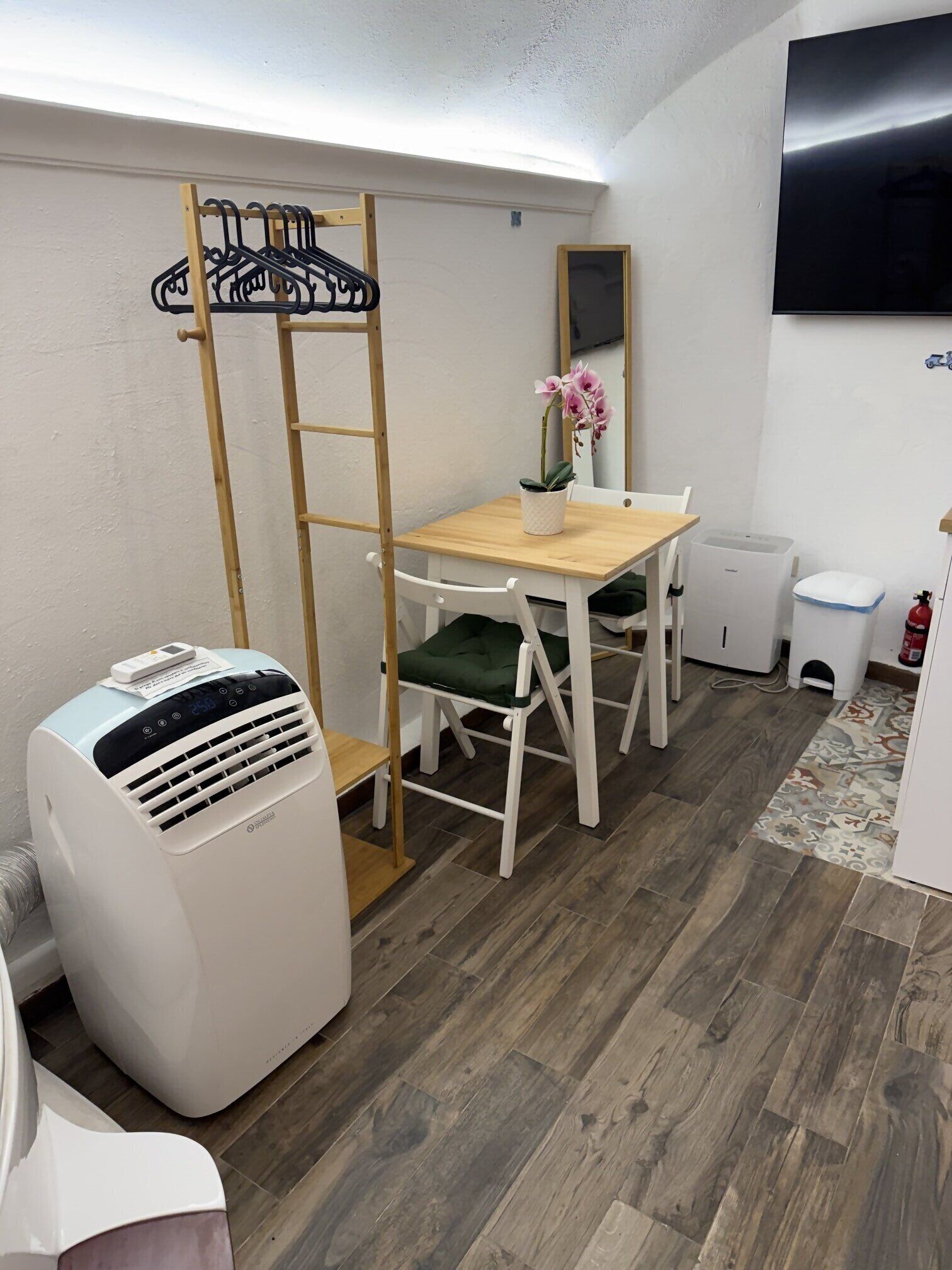 Ein Zimmer mit einem Holztisch, weißen Stühlen, einem Heizgerät, einem kleinen Topfpflanzen und einem Feuerlöscher.