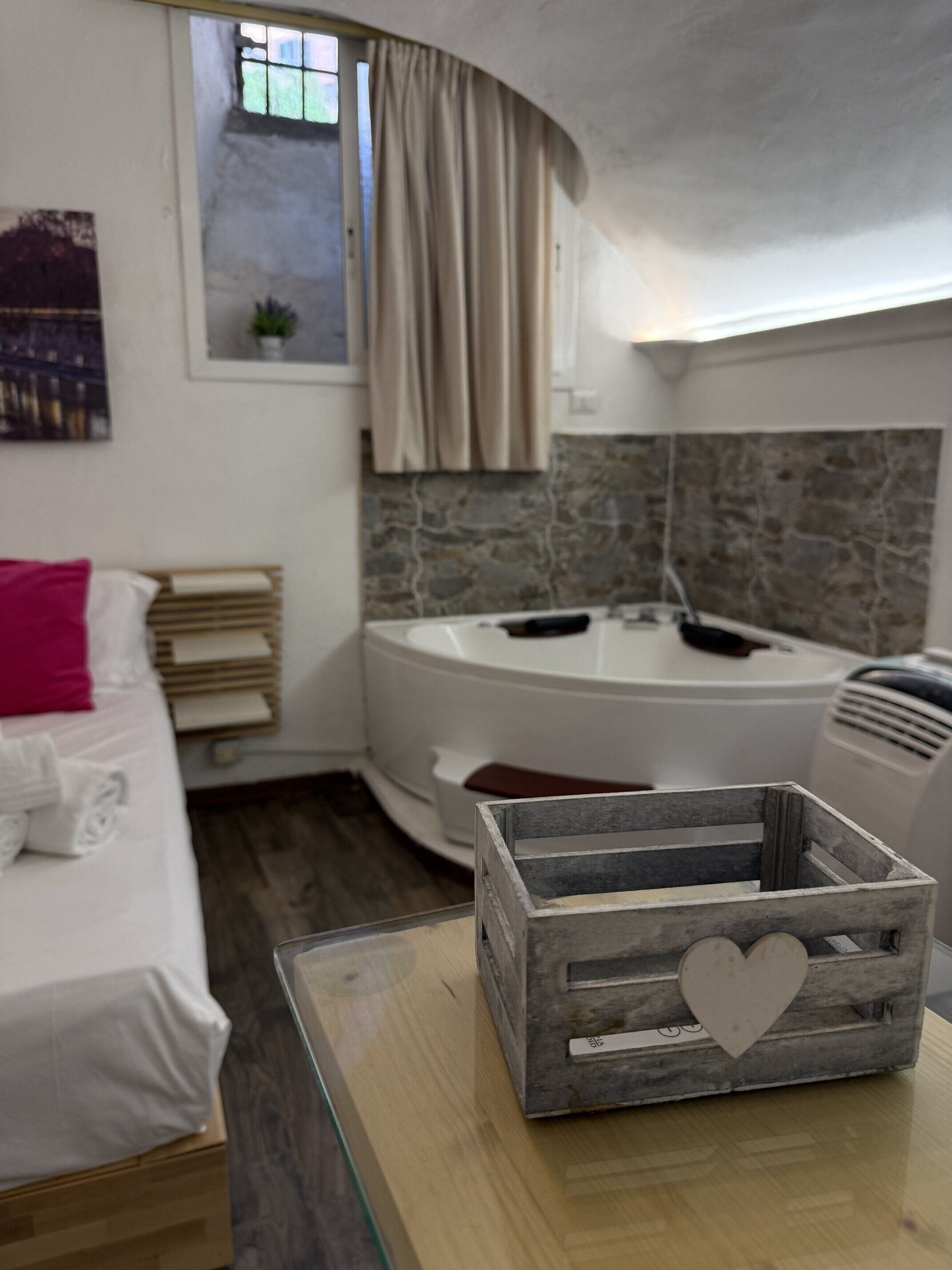 Ein Zimmer mit einem Bett, einem Nachttisch aus Holz, einer Badewanne und einer Steinwand.