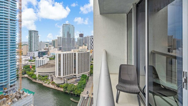 A high-rise building with a view of a city skyline, a balcony with a chair, and a river. - Luxe Condo on Miami River (Miami)