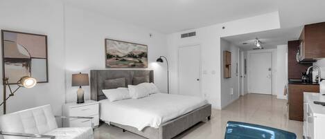 Quarto moderno com uma cama, mesas de cabeceira, uma cadeira, um quadro e vista para a cozinha.
