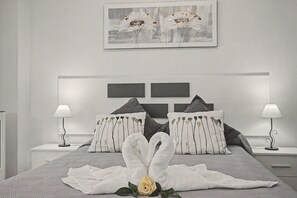 Un dormitori modern amb un llit gran, dues làmpades de nit i una obra d'art emmarcada sobre el llit.