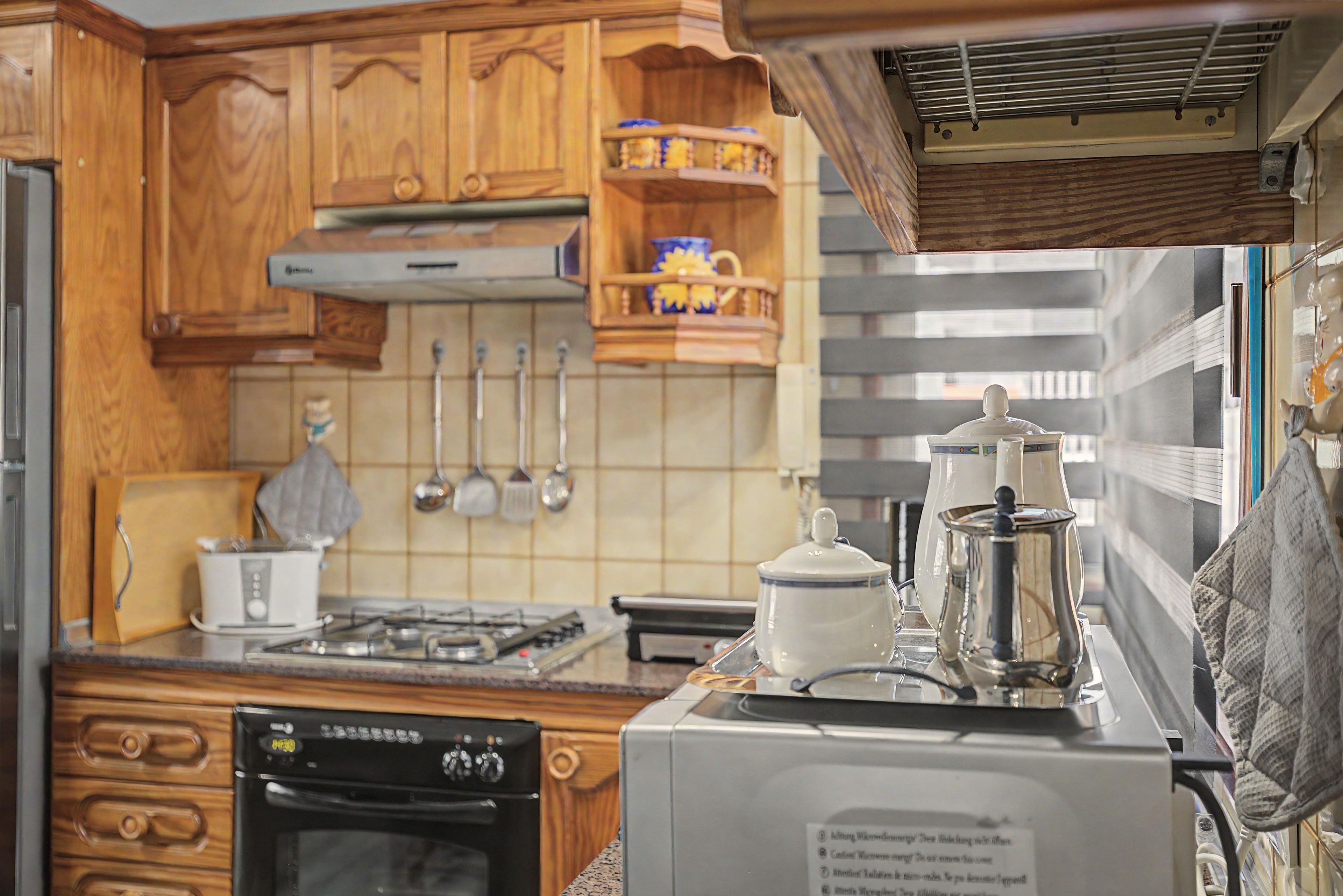 Cocina compacta con armarios de madera, estufa a gas, horno empotrado y cafetera.