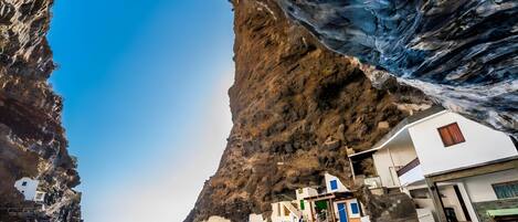 A coastal building with a large rock arch, a sea view, and a staircase leading to the entrance.
