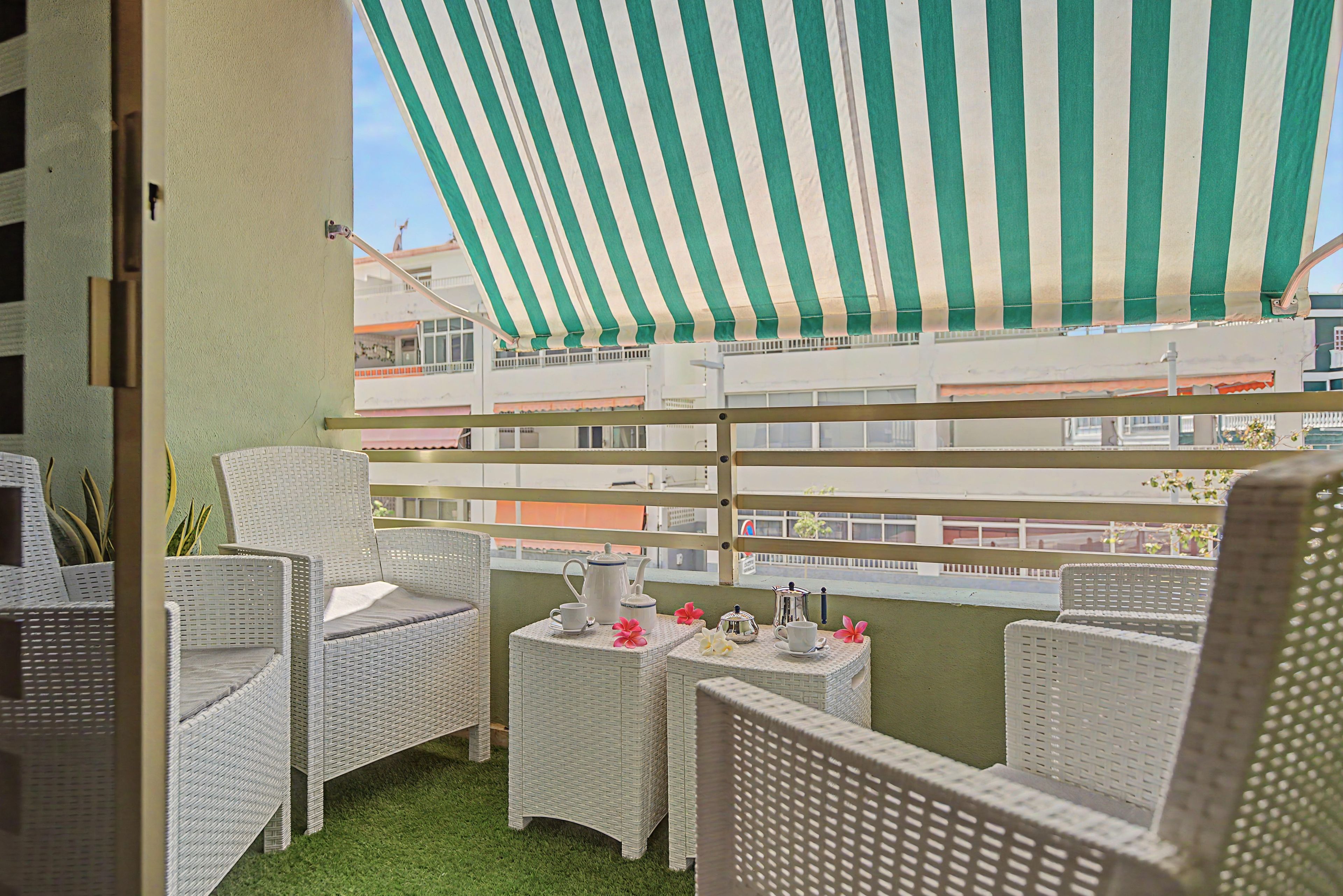 Un balcón con mobiliario de mimbre, un toldo a rayas y vistas a edificios.