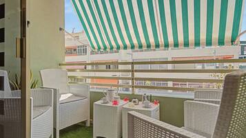 Un balcón con mobiliario de mimbre, un toldo a rayas y vistas a edificios.