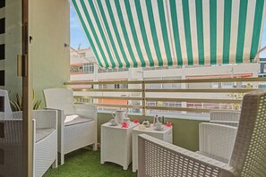 Un balcó amb moble de vimet, una estoreta estriada i vista a edificis.