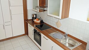 A compact kitchen with white cabinets, a built-in oven, a coffee maker, and a stainless steel sink. - SeeZeit Dingelsdorf - Modern Vacation Rental with Lake Views and Access to Bicycle Trails (Konstanz)