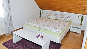 A bedroom with a sloped ceiling, a bed with floral bedding, a bedside table, a nightstand, and a small plant. - SeeZeit Dingelsdorf - Modern Vacation Rental with Lake Views and Access to Bicycle Trails (Konstanz)