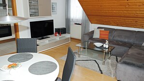 A modern living room with a television, sofa, and a dining area with a glass table. - SeeZeit Dingelsdorf - Modern Vacation Rental with Lake Views and Access to Bicycle Trails (Konstanz)
