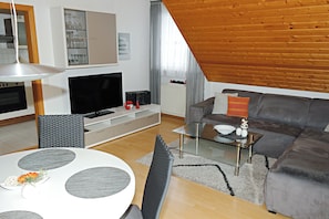A modern living room with a television, sofa, and a dining area with a glass table. - SeeZeit Dingelsdorf - Modern Vacation Rental with Lake Views and Access to Bicycle Trails (Konstanz)