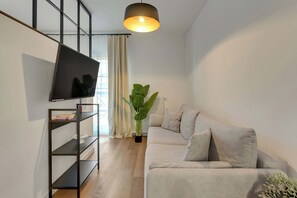 Ein modernes Wohnzimmer mit Flachbildfernseher, einer schwarzen Regallösung, einem grauen Sofa und einer großen Topfpflanze.