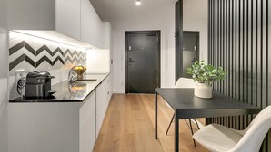 A modern kitchen with a Nespresso machine, a sink, and a countertop. There is a dining area with a table and a chair, and a potted plant. - Dwie Motławy 59 | Riverside | Perfect Stay (Gdańsk)