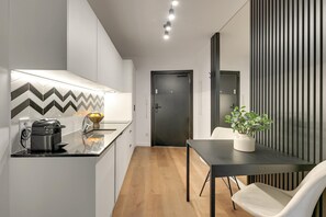 Eine moderne Küche mit einer Nespresso-Maschine, einem Spülbecken und einer Arbeitsfläche. Ein Essbereich mit Tisch und Stuhl sowie ein Topfpflanzen sind ebenfalls vorhanden.