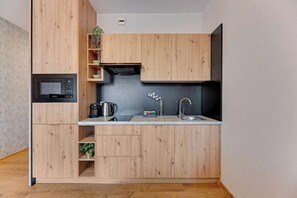 A compact kitchen with wooden cabinetry, a built-in microwave, a kettle, and a sink. - City Center | Bastion Wałowa 59 with Balcony (Gdańsk)