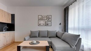 Una sala de estar moderna con un sofá seccional gris, una mesa de centro de madera y una cocina con un armario negro y un lavamanos.