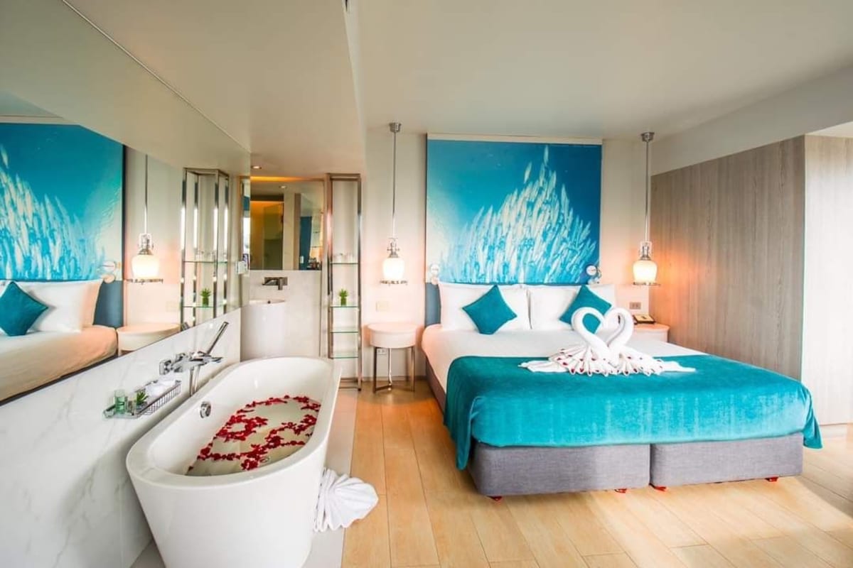 A modern hotel room with a large bed, a bathtub with rose petals, and a large window.