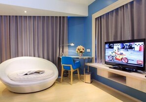 A modern hotel room with a round white chair, a desk with a chair, a television, and curtains. - J Tower Pattaya (Pattaya)