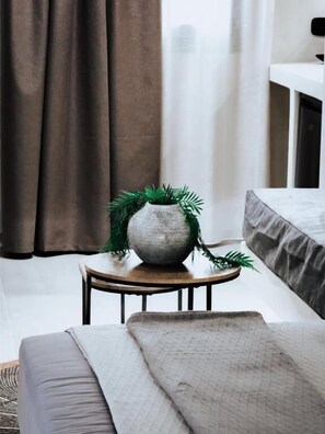 A room with a bed, a small round table with a potted plant, and a window with curtains. - Nonna's Suites (Naxos)