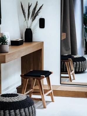 Ein Zimmer mit einem Holztisch, einem schwarzen Hocker, einem Spiegel und einer Topfpflanze.