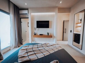 Un dormitorio moderno con cama, televisor montado, estante empotrado y puerta que da a un baño.