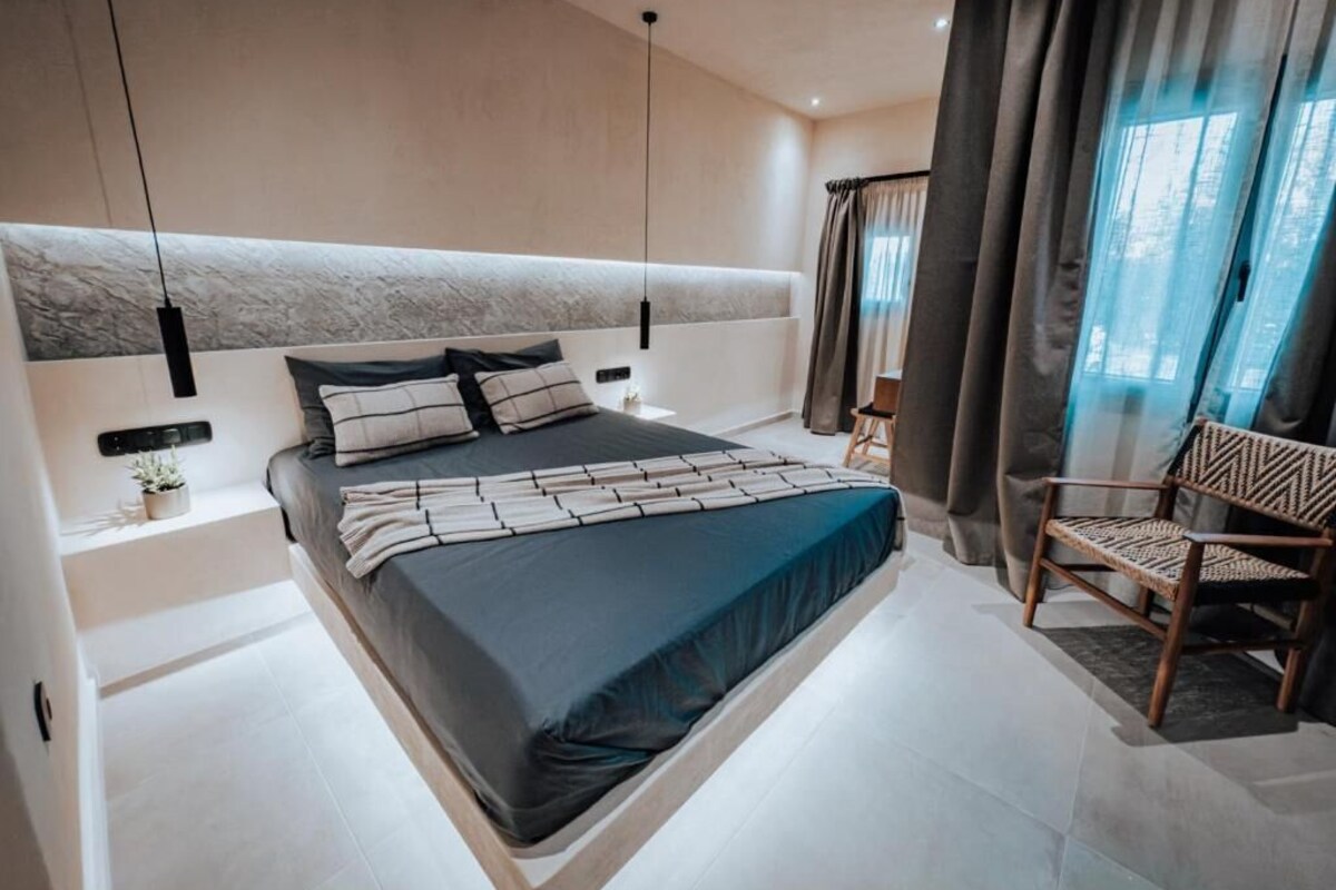 A modern bedroom with a large bed, bedside tables, a chair, and a window with curtains.