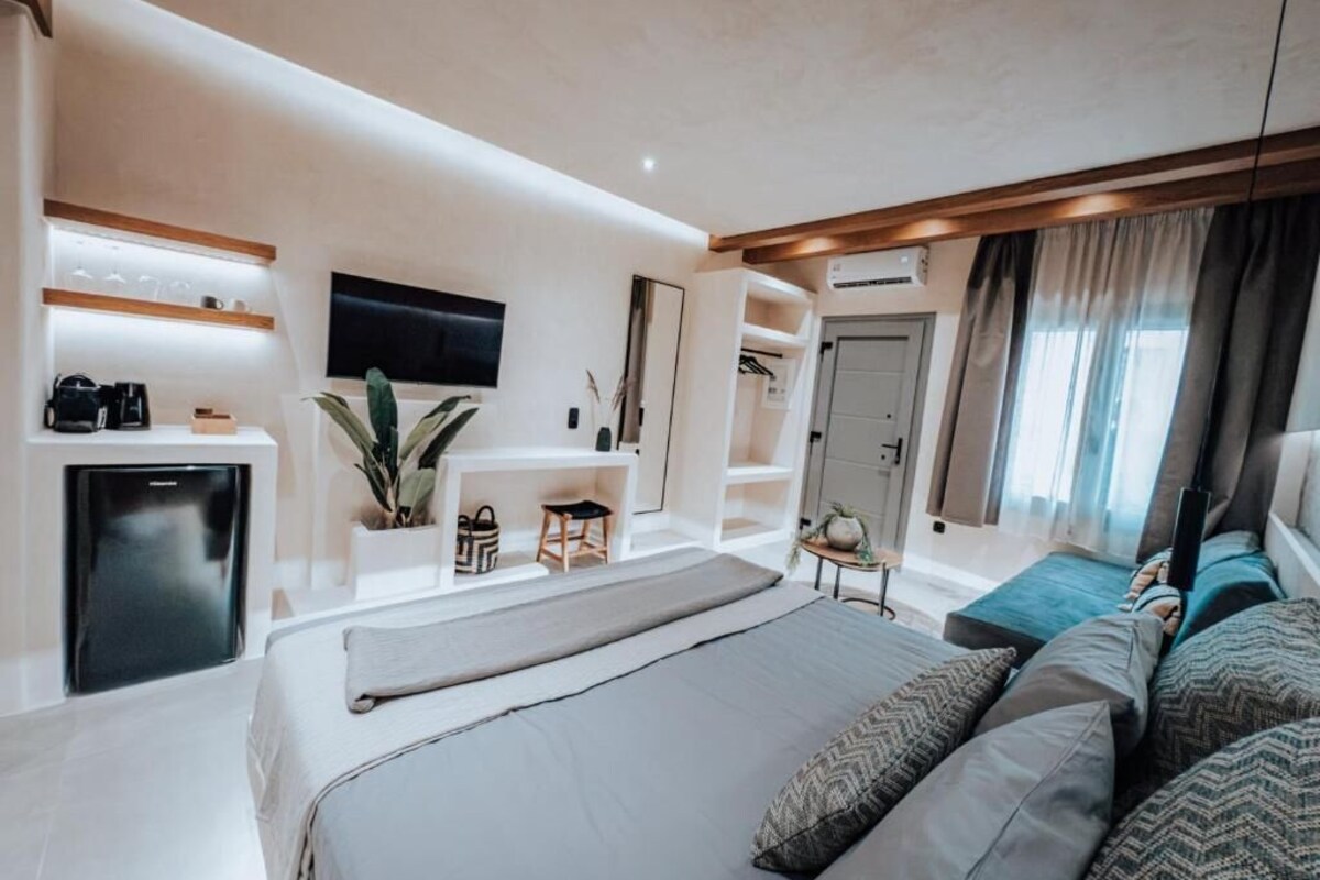 A modern hotel room with a large bed, a desk, a television, and a wardrobe.