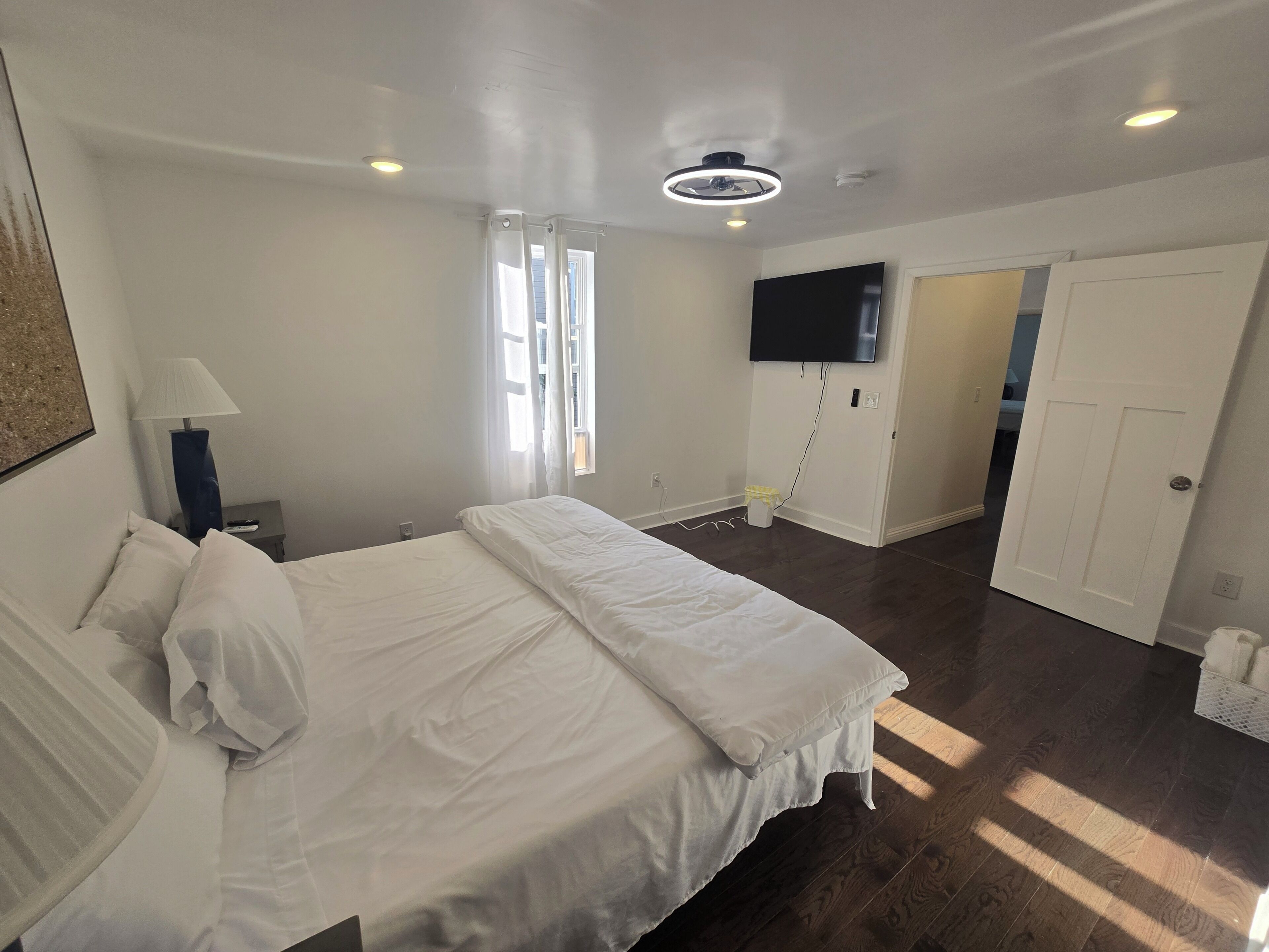 A hotel room with a bed, a television, a ceiling fan, and a door leading to another room.