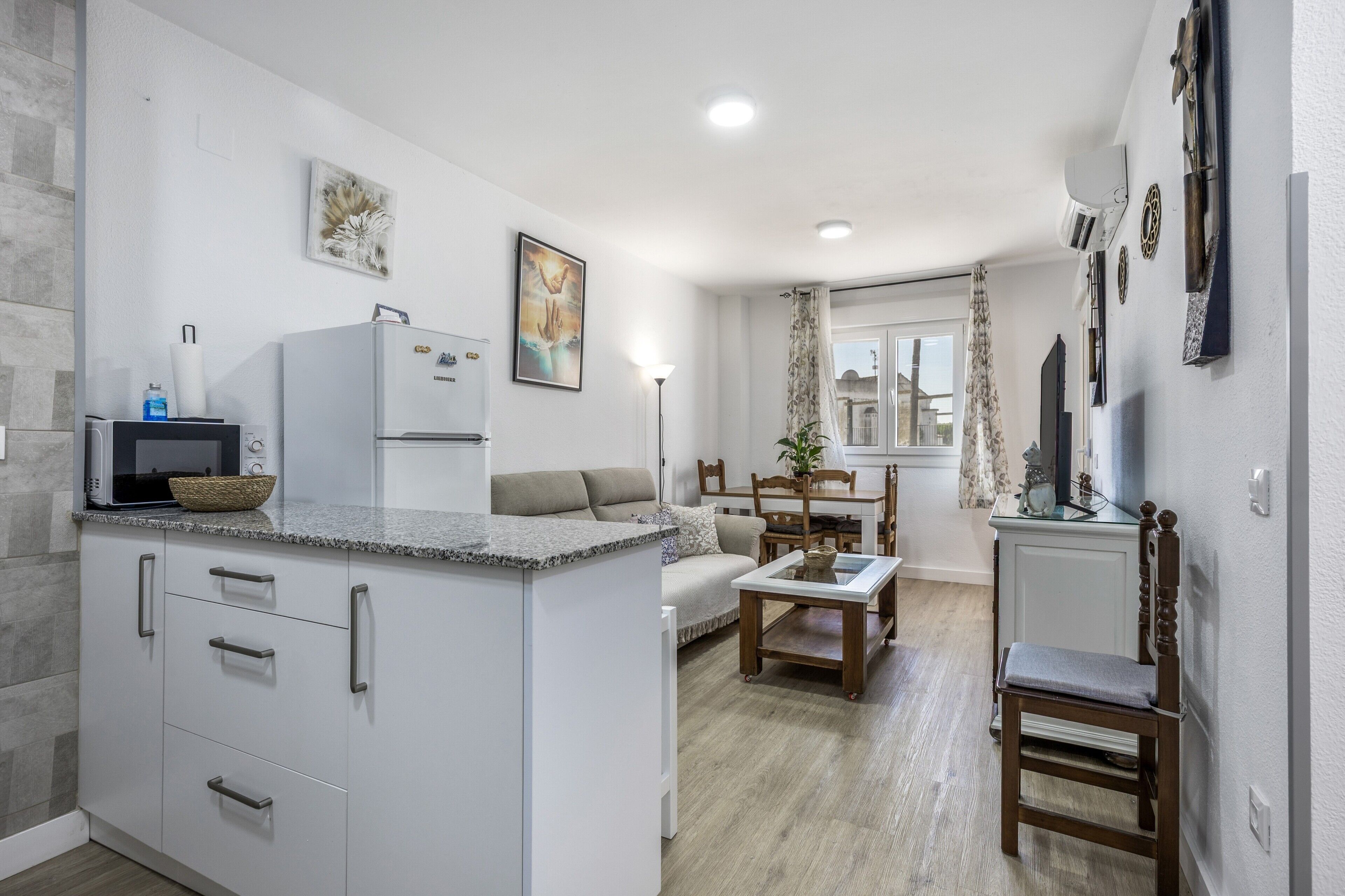 A modern kitchen with a built-in island, a dining area with a table and chairs, and a living space with a sofa and a TV.
