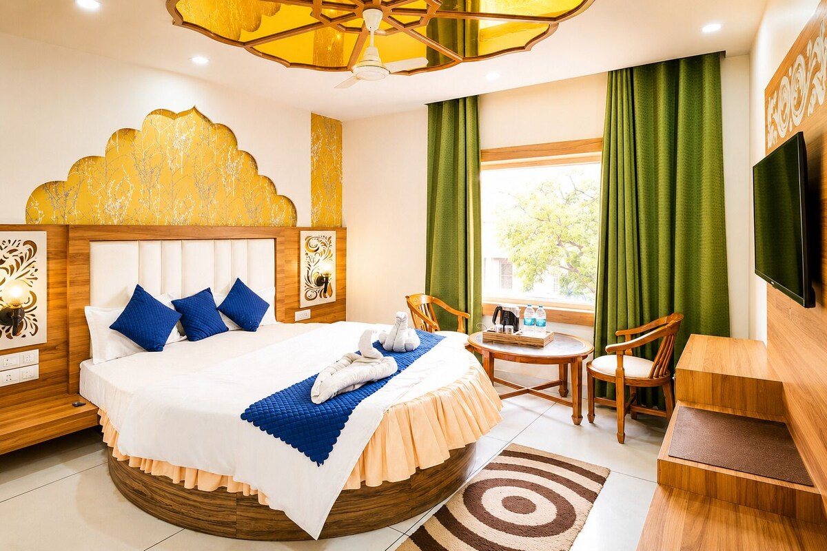 A hotel room with a round bed, a desk, a chair, a television, and a window with curtains.