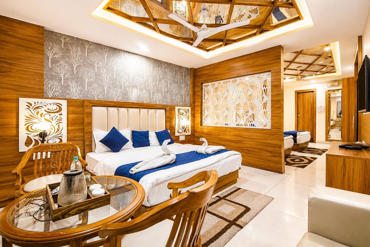 Habitación de hotel con una cama grande, un área de descanso con una mesa y sillas, un televisor y un panel decorativo en la pared.